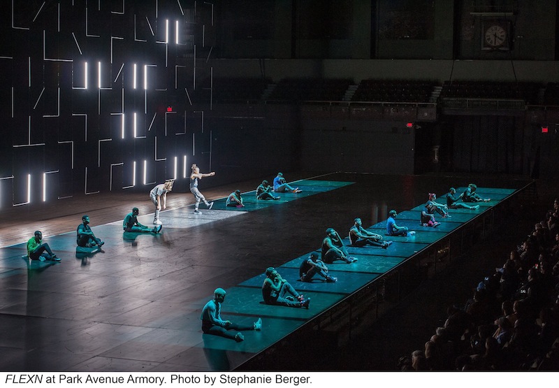 Two lines of seated FLEXN dancers, each in their own pool of light which denotes a prison scene